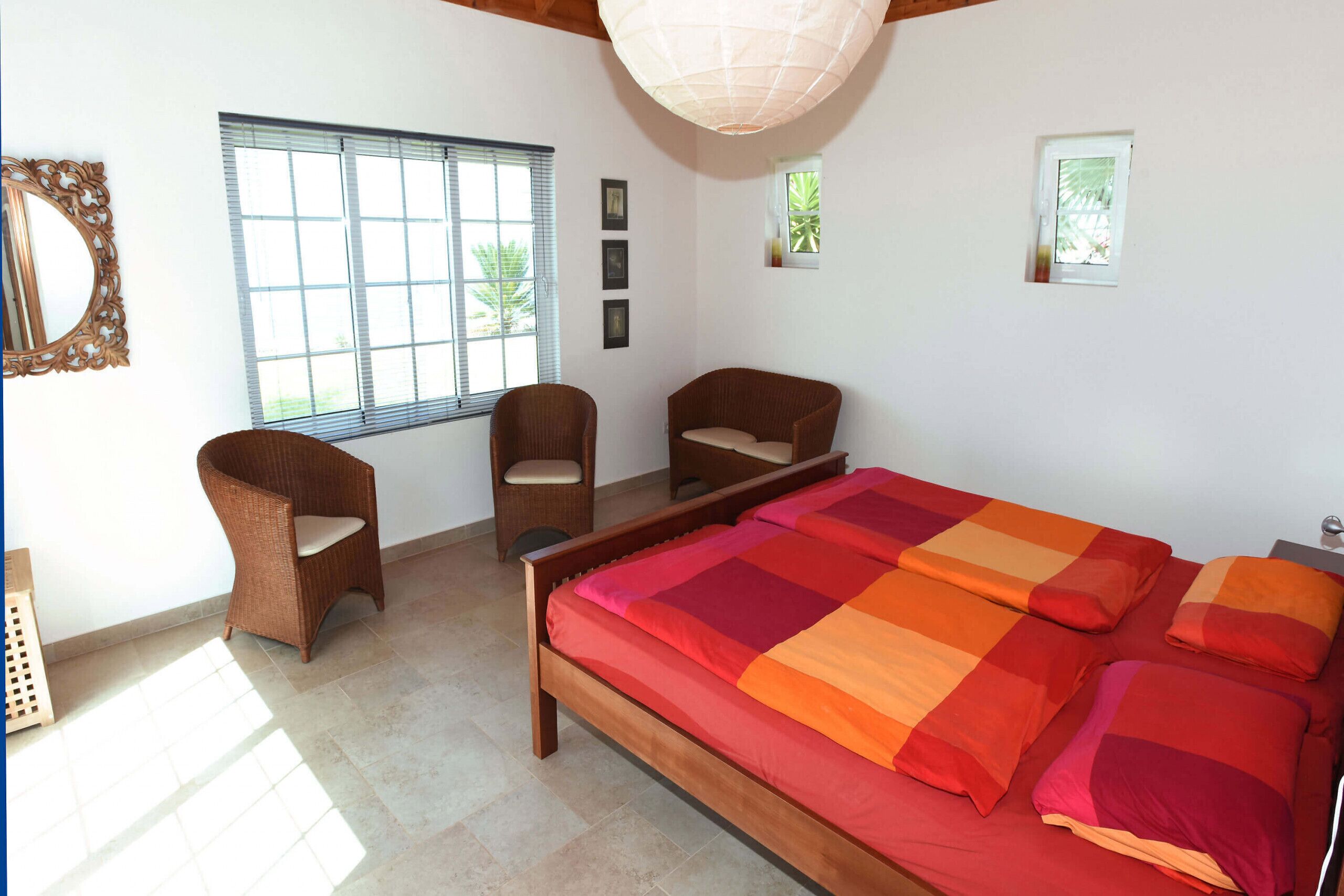 A bedroom with a large bed, two chairs, a window, and a ceiling light.