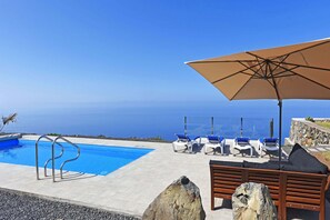 Ein Poolbereich mit Blick auf den Ozean, Liegestühle und eine Holzbank.