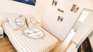 Et soveværelse med seng, puder, et natbord, et vægmonteret fjernsyn og et billede.