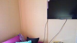 A room with a purple sofa, a small black TV on the wall, and a small black heater on the floor. - Golden Mount Rest, 9 guest's max, 1 Double, 7 Singles  (Mount Morgan)