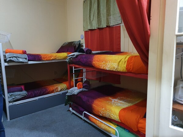 A dormitory room with bunk beds, a small shelf, and a window with curtains. - Golden Mount Rest, 9 guest's max, 1 Double, 7 Singles (Mount Morgan)