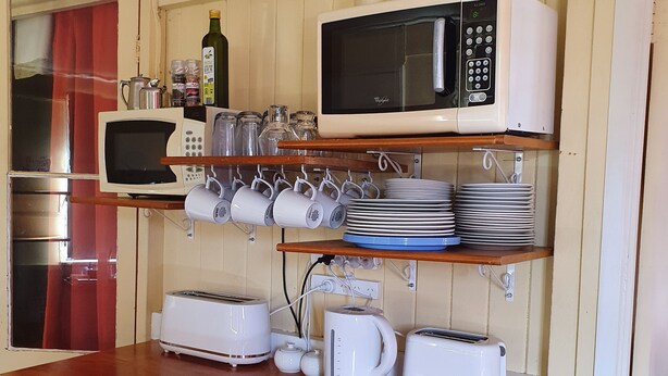 A compact kitchen with a microwave, toaster, kettle, and various kitchen utensils on shelves and counters. - Golden Mount Rest, 9 guest's max, 1 Double, 7 Singles  (Mount Morgan)