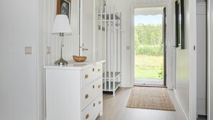 A hallway with white walls, a white dresser with gold handles, a lamp, and a basket. There is a door leading outside with a view of greenery. - Nice home in Torsby with kitchen (Torsby)