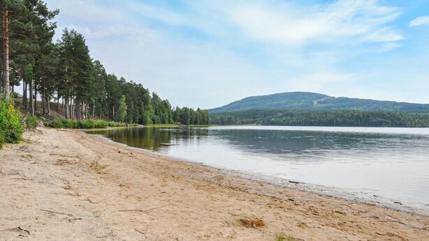 A sandy beach with a calm lake and a forested hill in the background. - Nice home in Torsby with kitchen (Torsby)