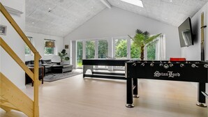 Un'ampia stanza con un tavolo da calcio, un'ampia finestra vista su vegetazione e un moderno design del soffitto.