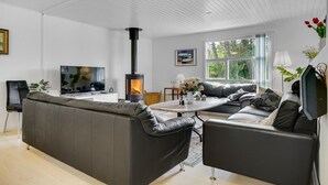Un soggiorno moderno con un divano, due poltrone, una TV, un caminetto e un'ampia finestra vista alberi.