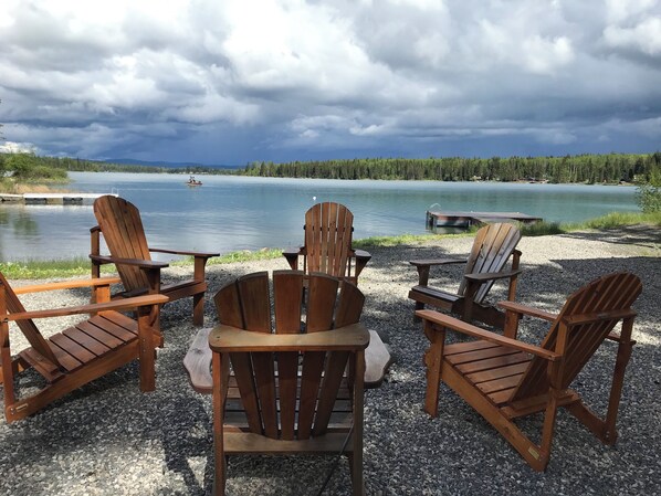 A lakeside seating area with wooden chairs and tables, a dock, and a boat. - Gorgeous Lakefront cabin, pet friendly! (Sheridan Lake)