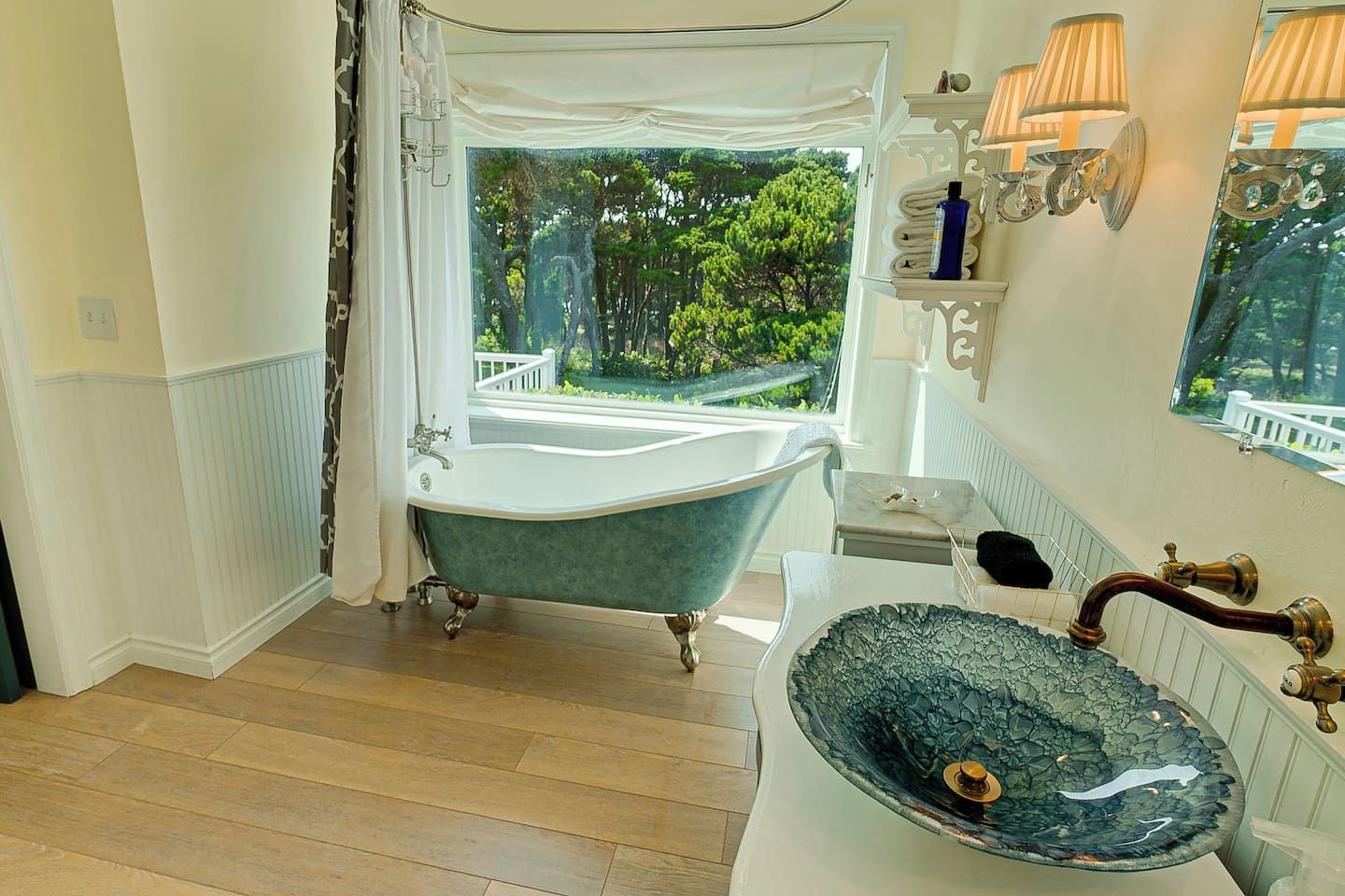 Une salle de bain avec une baignoire îlot, un lavabo doté d’un receveur décoratif et une fenêtre donnant sur un paysage verdoyant.