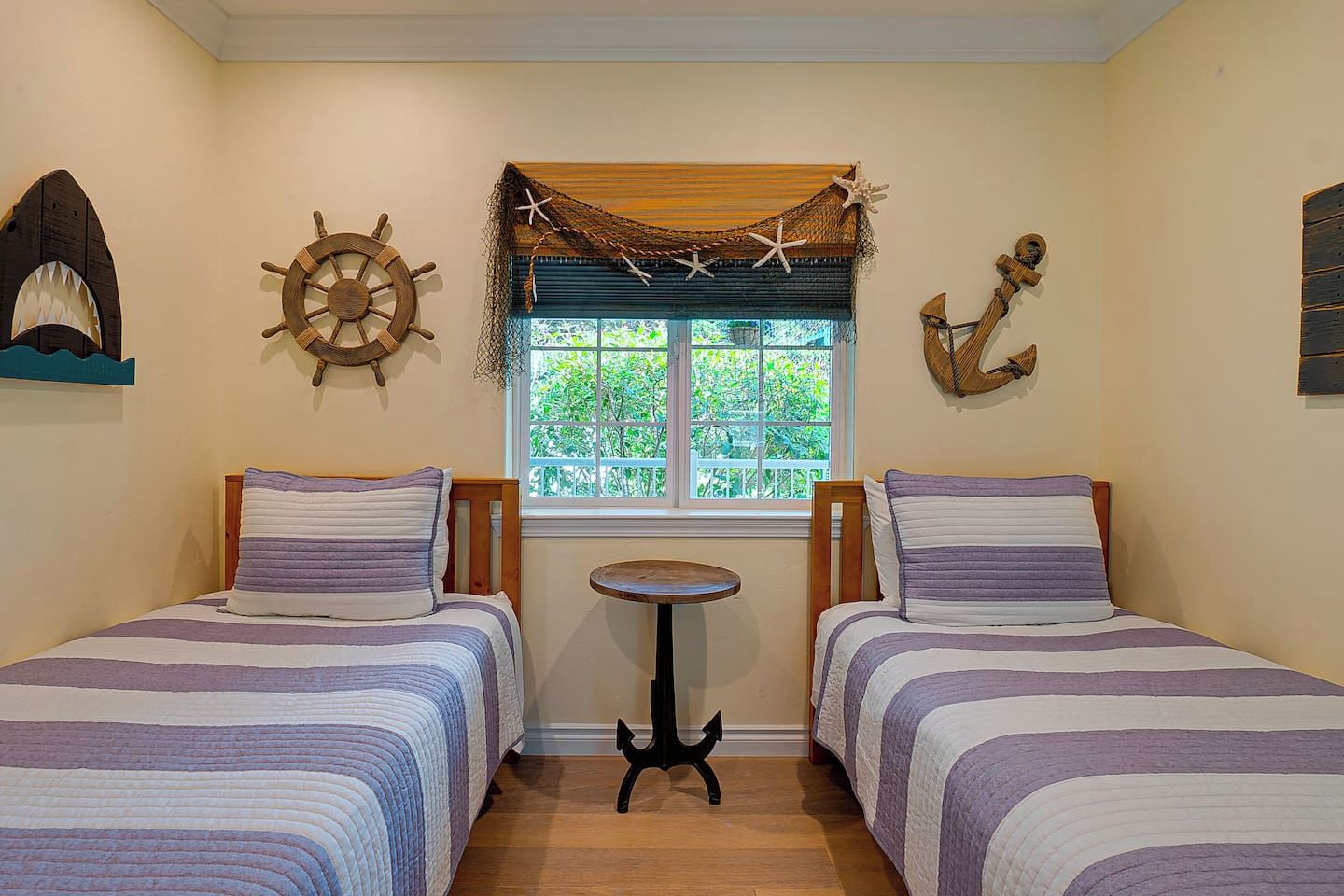 A room with two beds, a small table, and nautical decor including a ship's wheel and an anchor.