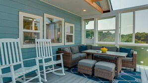 A sunroom with a blue exterior, wicker furniture, and large windows offering a view of greenery.