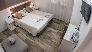 A modern hotel room with a neatly made bed, a small desk with a chair, a flat-screen TV, and a seating area with a cushioned bench. - Angel's Care B&B (Reggio Calabria)