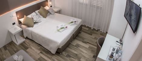 Une chambre d’hôtel moderne avec un lit soigneusement fait, un petit bureau avec une chaise, un téléviseur à écran plat et un coin salon avec un banc rembourré.