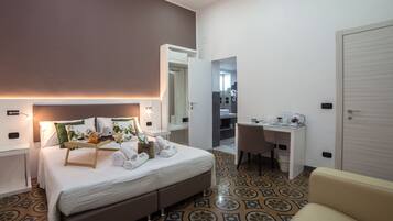 Ein modernes Hotelzimmer mit Bett, Nachttisch, Schreibtisch, Stuhl und einem durch eine offene Tür einsehbarer Badezimmer.