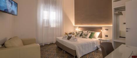 Una habitación de hotel con cama, mesita de noche, sillón, televisión y baño.