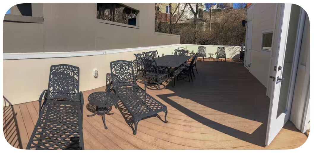 An outdoor patio with metal chairs and tables, a wooden deck, and a white building in the background.
