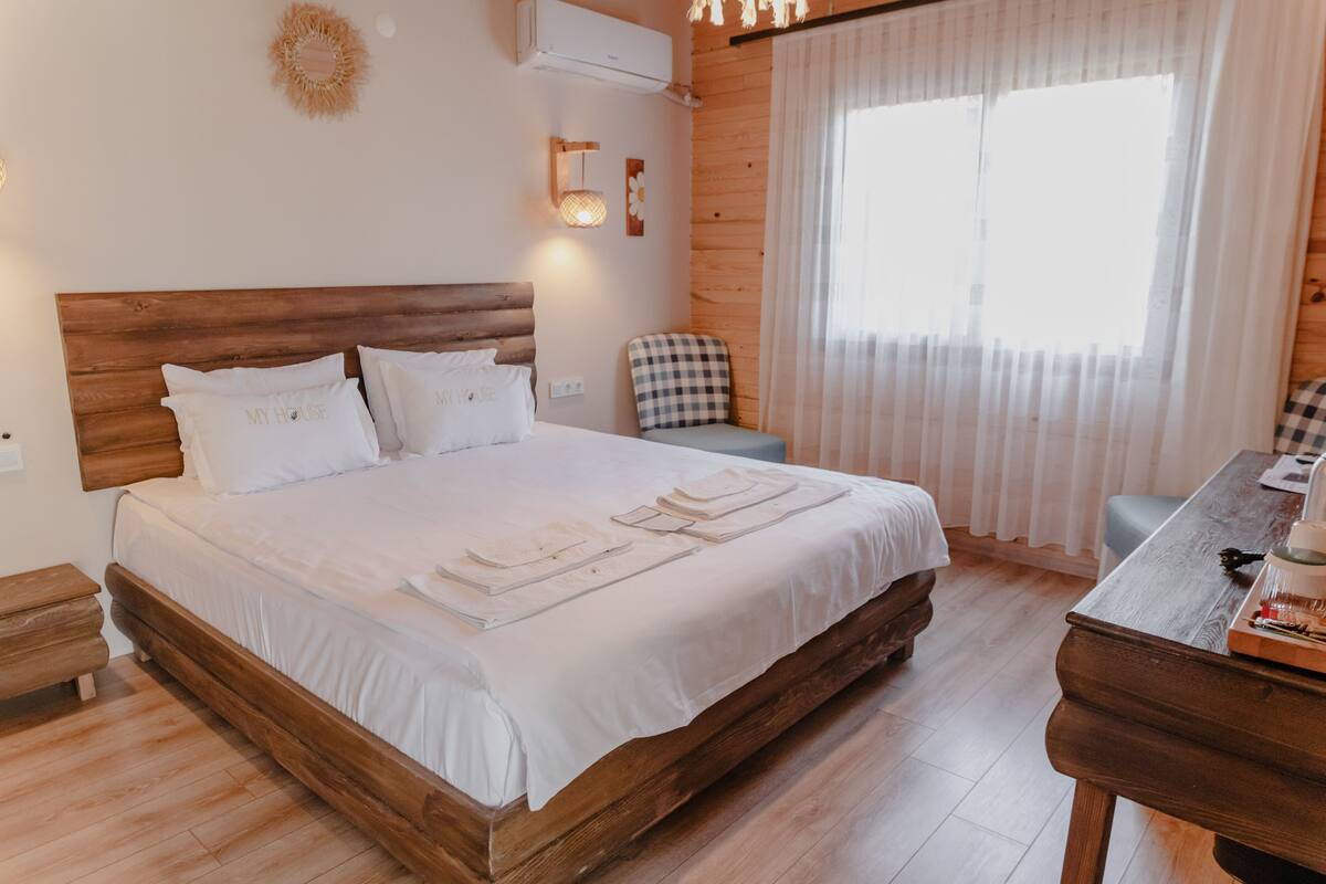 Een houten bed met witte beddengoed, een geruite stoel en een houten tafel met een dienblad.