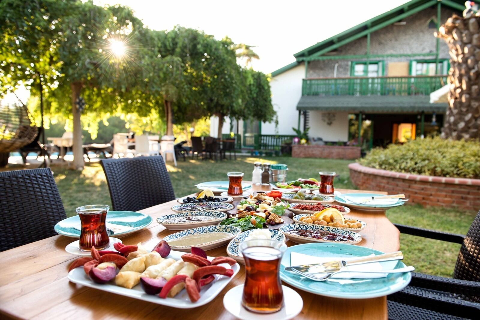 An outdoor dining area with a variety of dishes, including fruits, nuts, and bread, and a table set with plates, glasses, and cutlery.