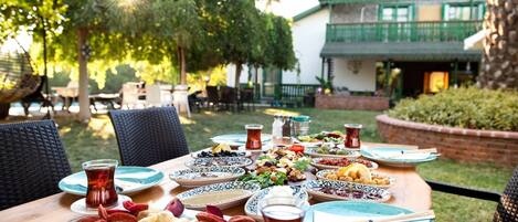 An outdoor dining area with a variety of dishes, including fruits, nuts, and bread, and a table set with plates, glasses, and cutlery.