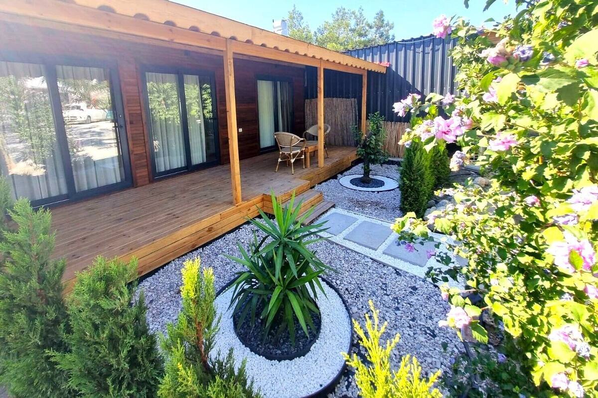 Een modern huis met een houten terras, een overdekte patio en een tuin met planten en bloemen.