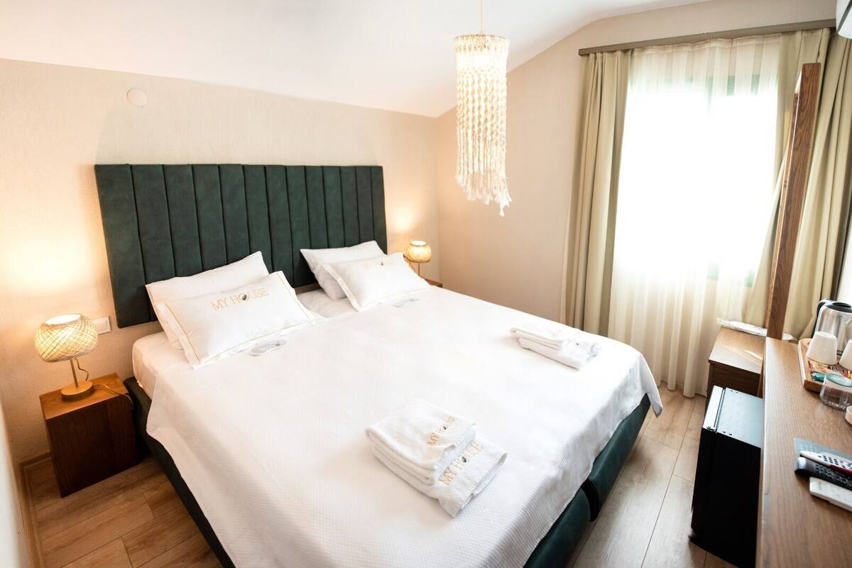 Hotelkamer met een groot bed, twee nachtkastjes, een kroonluchter en uitzicht op het omliggende landschap.