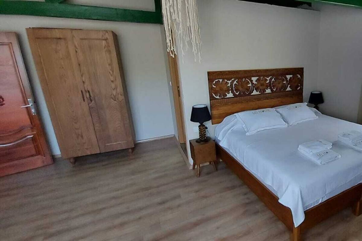 Een slaapkamer met een houten bed, witte beddengoed, een nachtkastje, een lamp, een kledingkast en een raam met gordijnen.