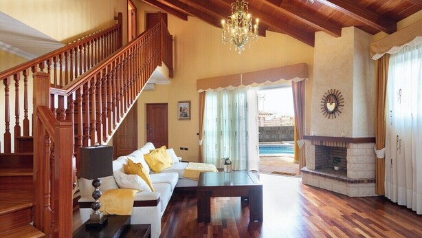 Ein geräumiges Wohnzimmer mit einer Holztreppe, einer Chandelüster, einem Kamin und einem großen Fenster mit Vorhängen.