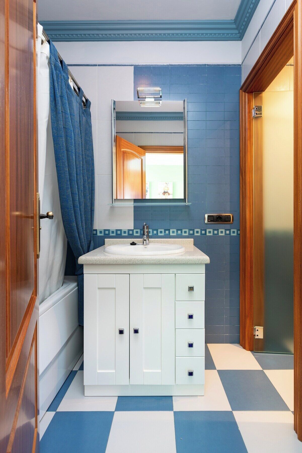 A bathroom with a white vanity, a mirror above the sink, and a blue and white checkered floor.