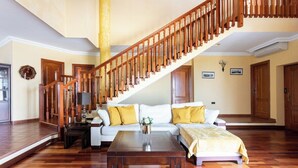 Ein geräumiges Wohnzimmer mit einer Holztreppe, einem weißen Sofa mit gelben Kissen und einem Holztisch.