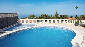 Ein Swimmingpool mit weiß-schwarz gemustertem Rand, umgeben von einem weißen Zaun und Palmen.