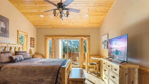 Ein Schlafzimmer mit Bett, Fernseher, Deckenventilator, Holzwänden und einem Balkon.