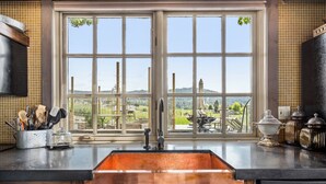 Una cocina con un ventanal grande, un lavamanos de cobre y vistas a un paisaje verde.