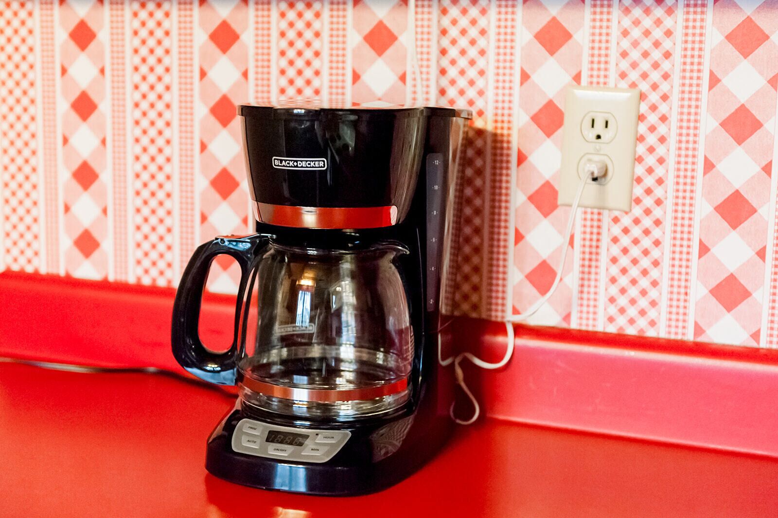 Eine BLACK+DECKER-Kaffeemaschine auf einer roten Arbeitsplatte, im Hintergrund eine Wand mit Musterung.