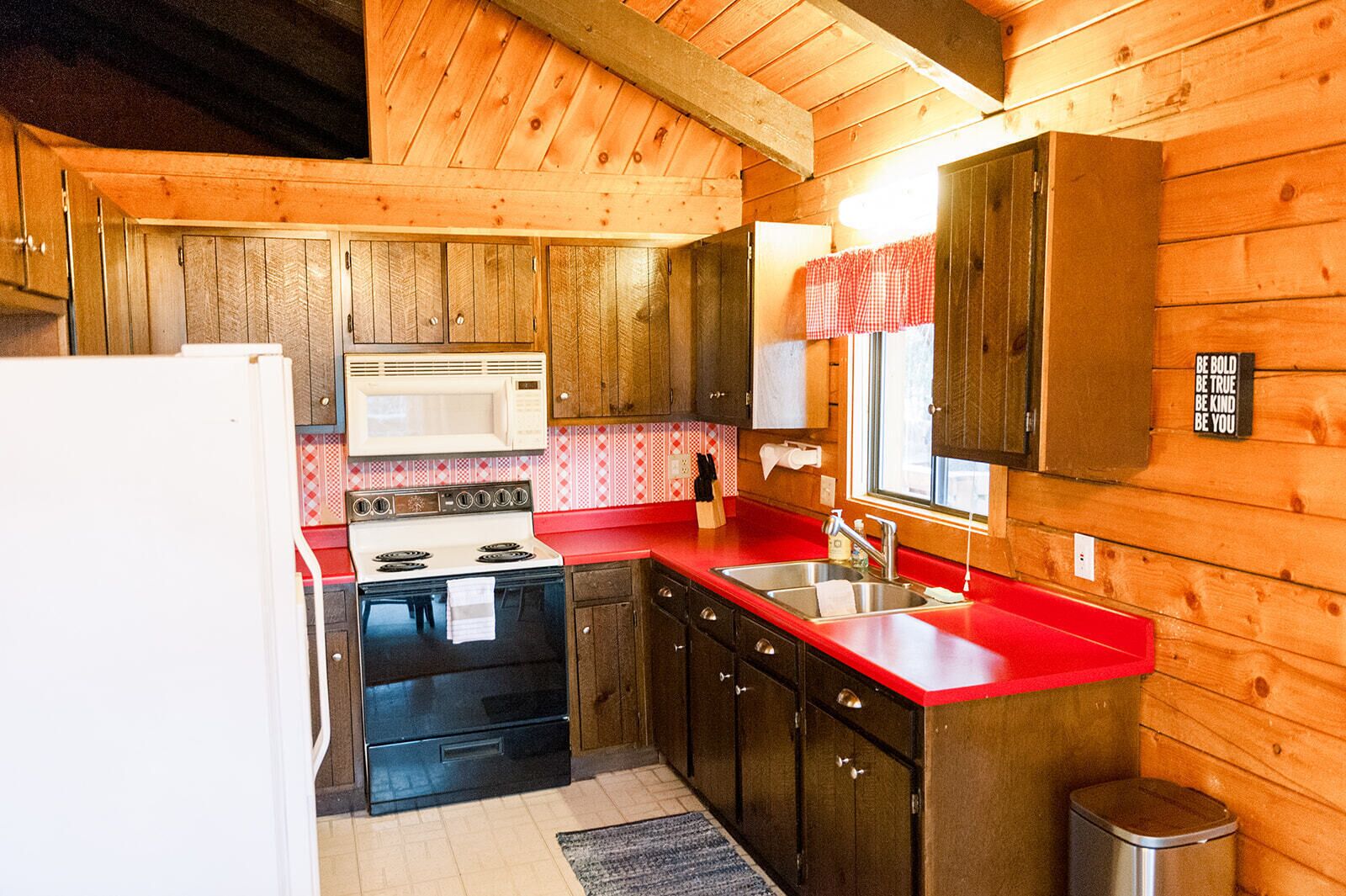 A compact kitchen with wooden walls, a red countertop, a white stove, and a microwave.