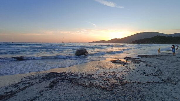 Une plage avec des vagues, des rochers et un coucher de soleil.