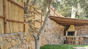 Un mur de pierres, une clôture en bambou, un petit arbre et une zone herbeuse parsemée de rochers.