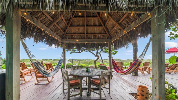 A wooden deck with a thatched roof, a round table with chairs, and hammocks.