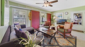 A living room with a sofa, armchair, coffee table, and a ceiling fan.