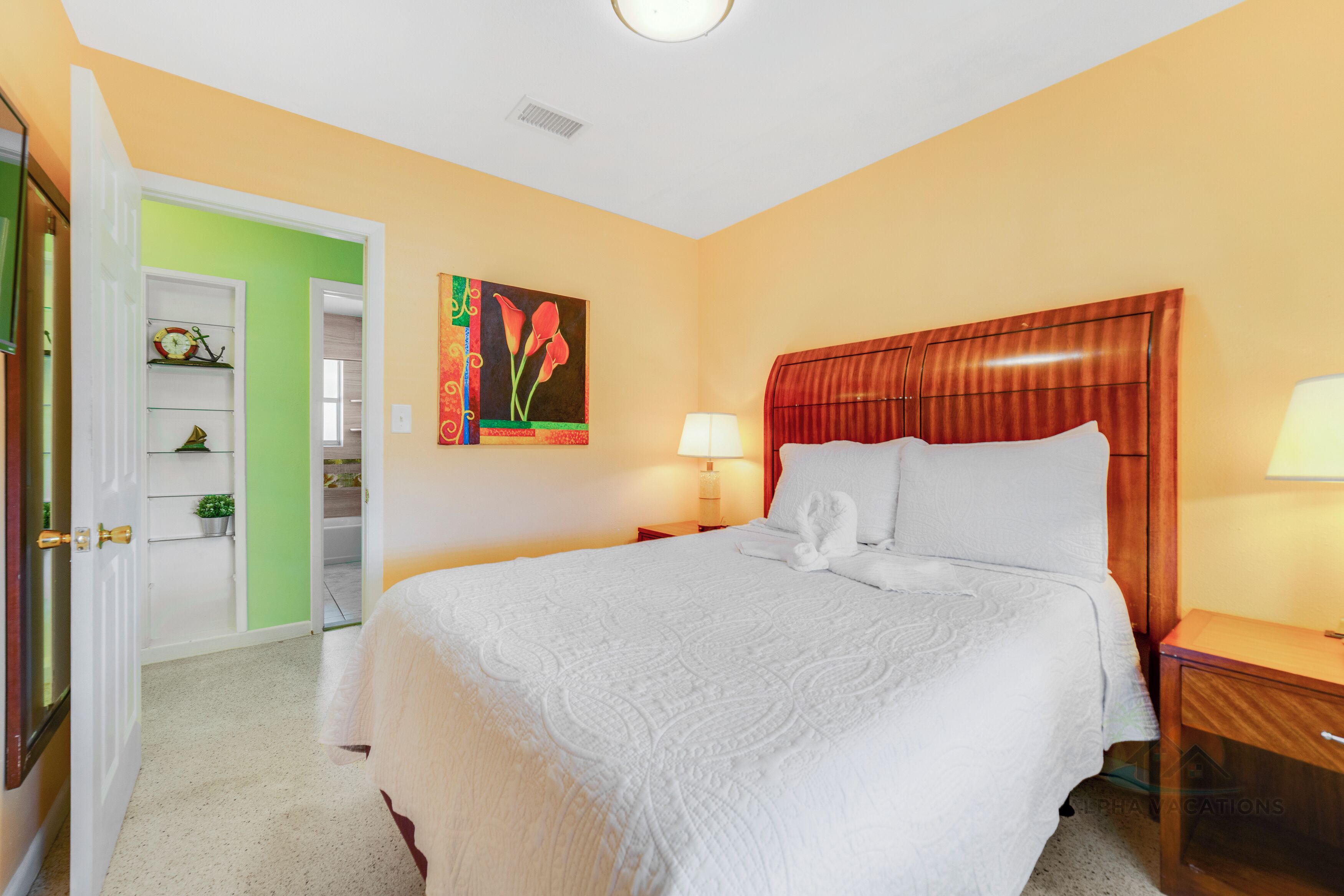 Une chambre d’hôtel avec un grand lit, une table de chevet, une lampe, un tableau au mur et une porte verte donnant sur un placard.