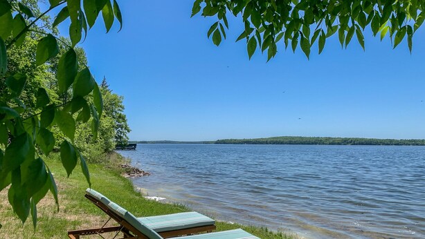 A lakeside view with a wooden lounge chair and a bench by the water. - Cozy Vintage Cabin on Lake Pokegama & MTB Trails (Cohasset)