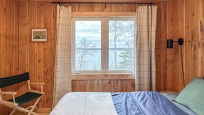A wooden room with a bed, a bench, and a window with a view of trees and a body of water. - Cozy Vintage Cabin on Lake Pokegama & MTB Trails (Cohasset)
