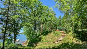 A cabin with a wooden staircase leading up to it, surrounded by trees and a lake. - Cozy Vintage Cabin on Lake Pokegama & MTB Trails (Cohasset)