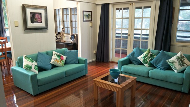 A living room with two teal sofas, a wooden coffee table, and a dining area with a wooden table and chairs. - At the Centre of Gallery Walk, Tamborine Mountain (Eagle Heights)