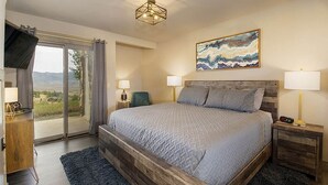 Een slaapkamer met een groot bed, een televisie, een bureau en uitzicht op het omliggende landschap.