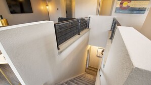 Een meerlaags interieur met een bekleed trappenhuis, een witte muur en een schilderij.