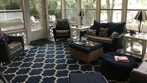 Una habitación iluminada por el sol con piso estampado, muebles de mimbre y vista a plantas.
