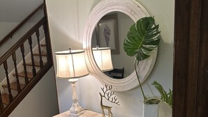 Una consola de madera con un espejo, dos lámparas, un adorno de ciervo y una planta en maceta frente a una pared.