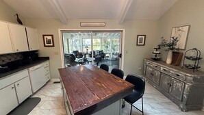 Una cocina con una isla grande, armarios blancos y un comedor con mesas al aire libre.