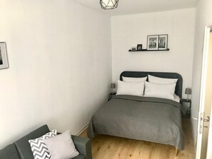 A bedroom with a bed, a bedside table, a lamp, a chair, and a wall-mounted shelf with pictures. - Luxury Condo (Leipzig)