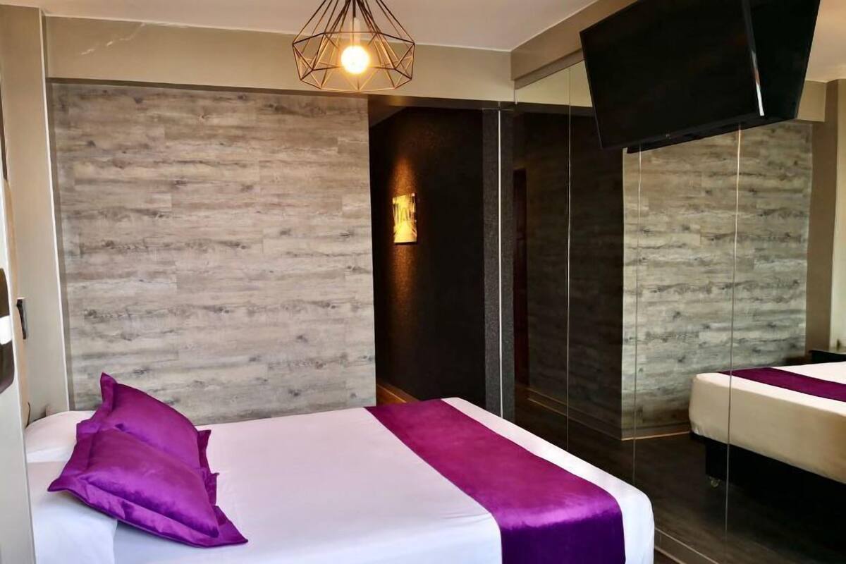 Una habitación de hotel moderna con una cama, un televisor y un espejo.