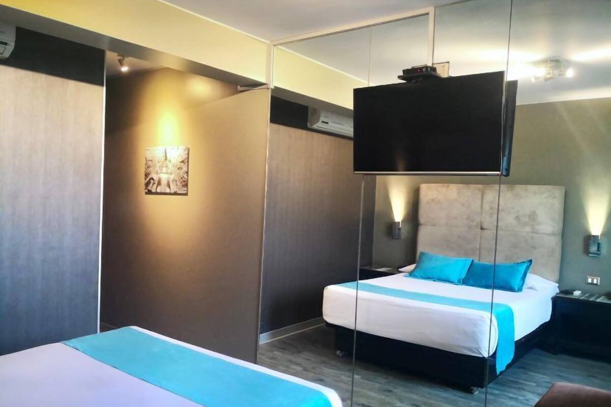 Habitación de hotel con una cama grande, una cama más pequeña, un televisor montado en la pared y un cuadro.